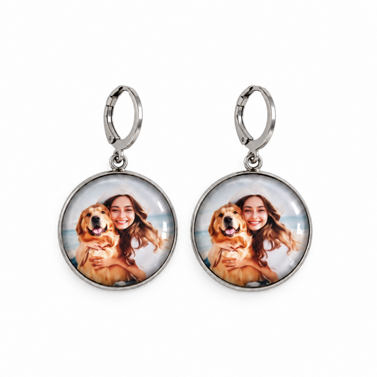 A pair of silver hoop drop earrings with oval face charms. Each charm features a custom printed photo of a woman holding a golden retriever dog, set in a silver bezel with a clear dome cover, shown against a plain white background.