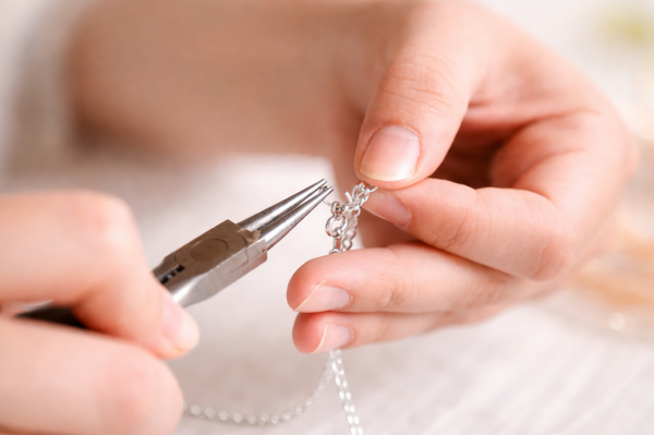 Close-up of hands using pliers to work on a piece of jewelry.